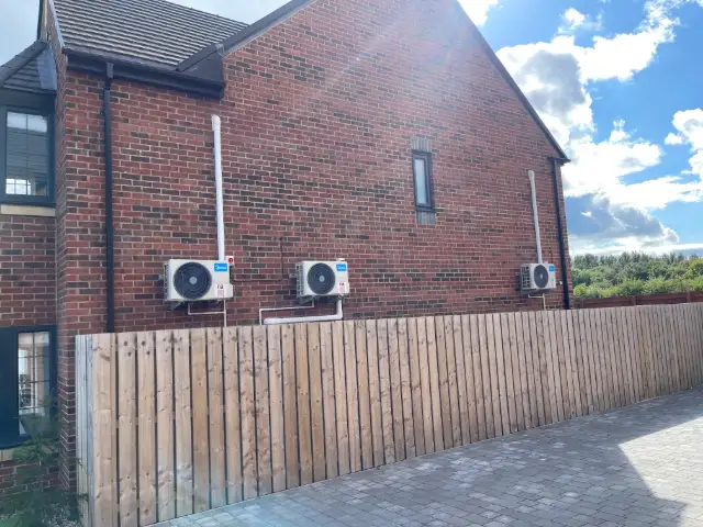 Two outdoor air conditioning units on a modern brick home behind a timber fence