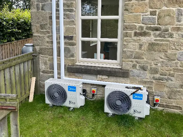 Outdoor air conditioning units on the lawn beside a stone cottage