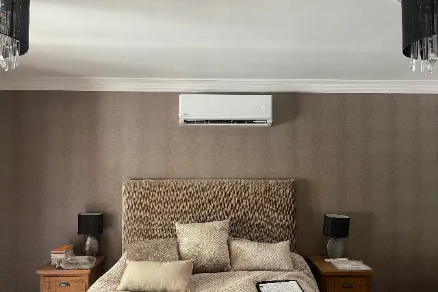 Quiet wall-mounted air conditioning unit installed above the bed in a calm, neutral bedroom