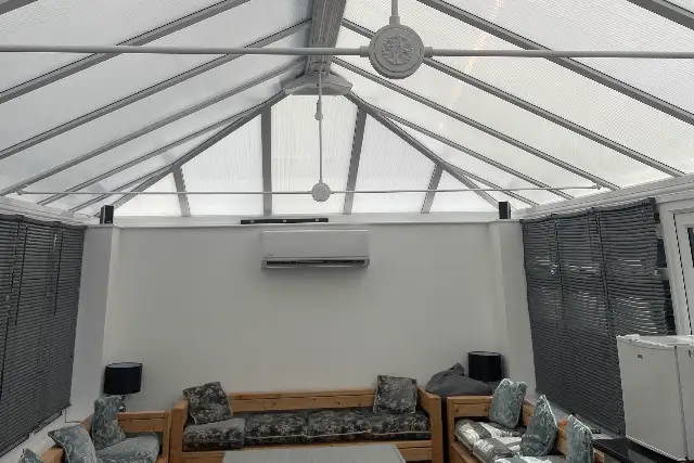 Air conditioning unit installed on the end wall of a glass-roofed conservatory