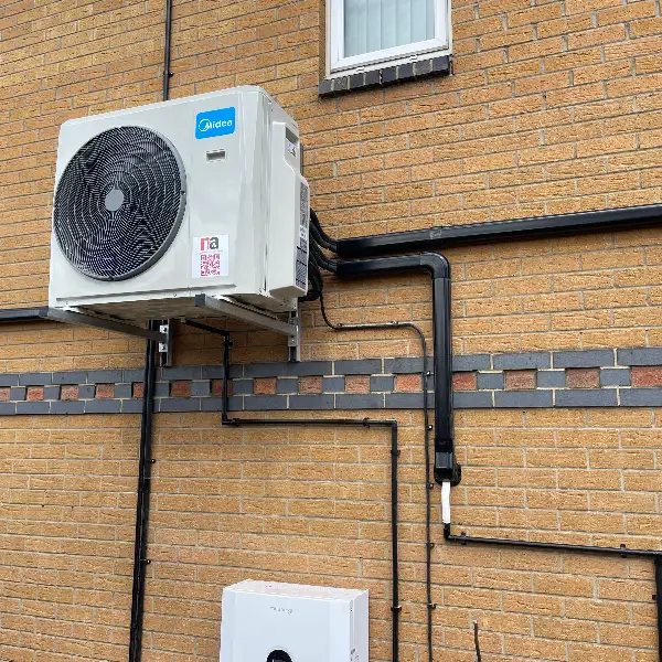 Outdoor air conditioning condenser with neat black pipe trunking on a brick wall