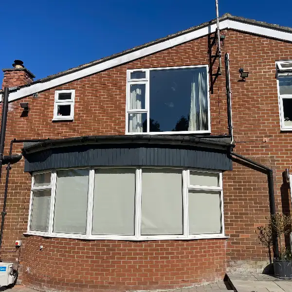 Outdoor air conditioning unit positioned discreetly at the rear of a two-storey brick house